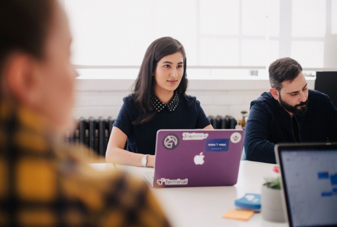 a young woman uses a laptop and listens to her colleagues