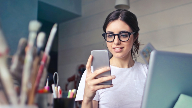 a woman using a phone and laptop with pens on her desk